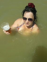 Portrait of woman holding beer while swimming in lake