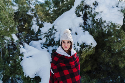 Portrait of woman standing against snow covered trees during winter