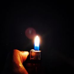 Close-up of hand holding lit candle in the dark