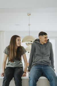 Smiling siblings sitting on kitchen island at home