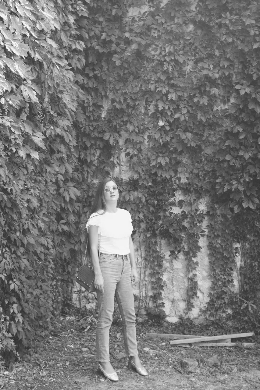 PORTRAIT OF WOMAN STANDING AGAINST PLANTS