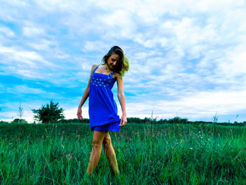 Smiling young woman posing on grassy field against cloudy sky