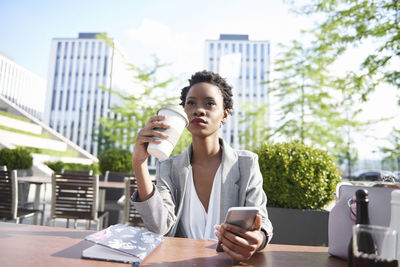 Portrait of businesswoman with cell phone drinking coffee at sidewalk cafe