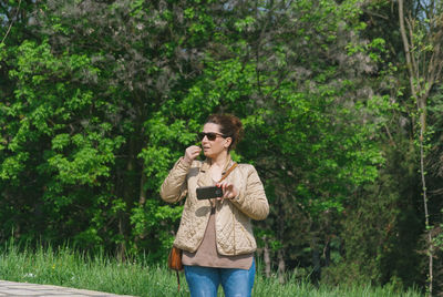 Young woman holding mobile phone while standing in forest