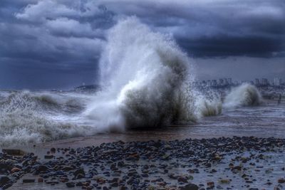 Waves splashing on rocks against cloudy sky