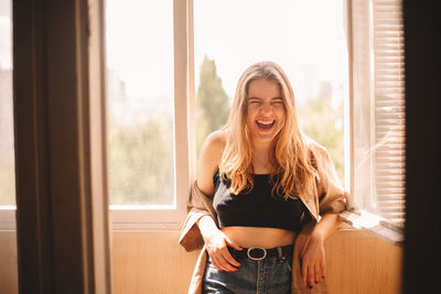 Young cheerful woman laughing while leaning in balcony during summer