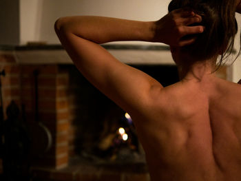 Rear view of shirtless woman standing against fireplace