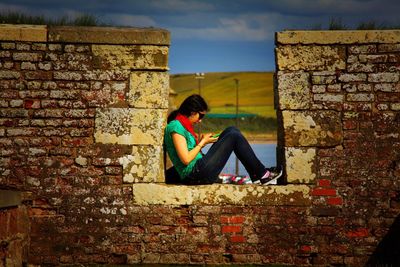 Side view of woman sitting against brick wall