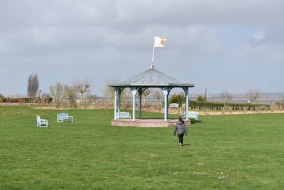 Rear view of woman walking on grass towards gazebo in park