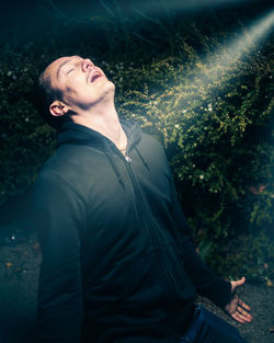 Man with eyes closed standing against plants with sunlight falling on face