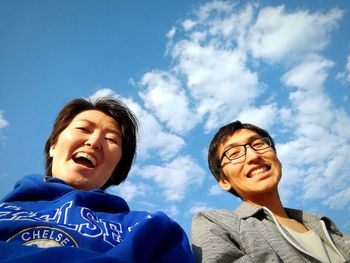 Low angle view of smiling young woman against blue sky