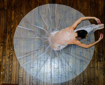 High angle view of ballerina wearing dress sitting on hardwood floor