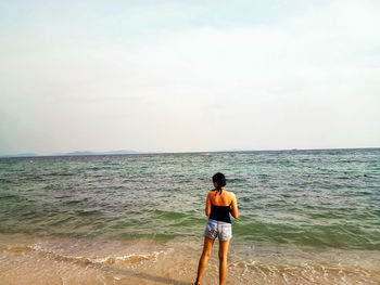 Rear view of man standing on beach against sky