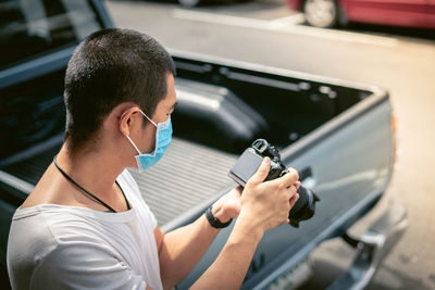 Side view of man wearing mask photographing with camera while standing outdoors