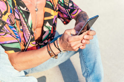 Crop view of hipster man sitting on the ground chatting on social media via mobile phone on sunny day