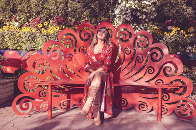 Young woman sitting on bench against plants