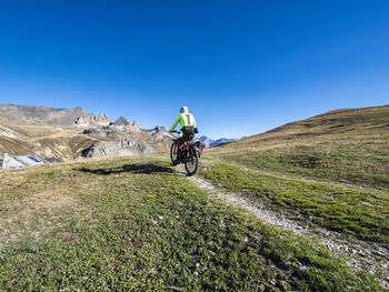 Man riding mountain bike on trail under blue sky, vanoise national park, france