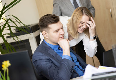 Beautiful woman pointing at laptop  and discussing  with her coworker while standing at office