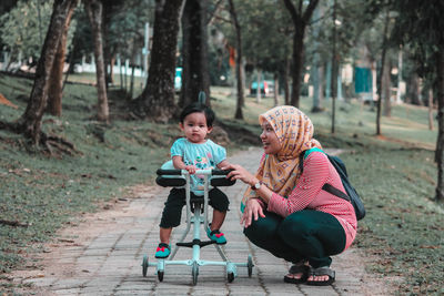 Smiling woman with daughter on toy scooter playing in park
