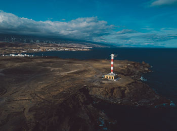 Lighthouse amidst sea and buildings against sky