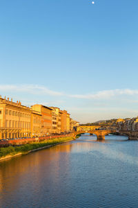 Bridge over river by buildings against blue sky