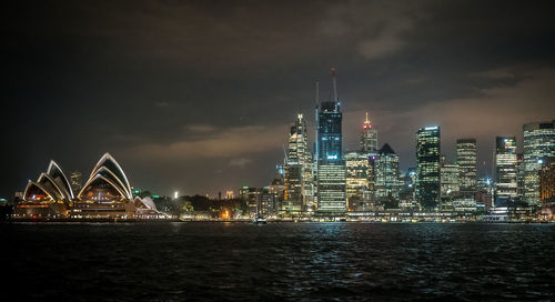 Illuminated city by river against sky at night