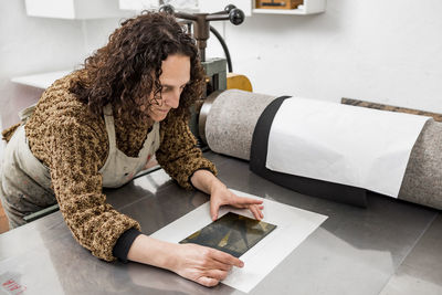 Female artist operating a manual vintage industrial printer.