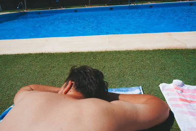 Shirtless man lying on grass by swimming pool