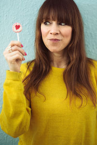 Woman having lollipop while standing against wall