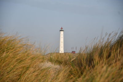 Lighthouse on field by sea against sky