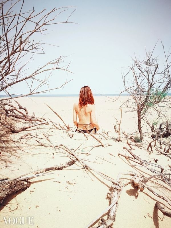 WOMAN SITTING ON BARE TREE