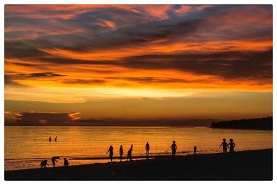 Silhouette people at beach against sky during sunset