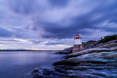 Lighthouse by sea and buildings against sky