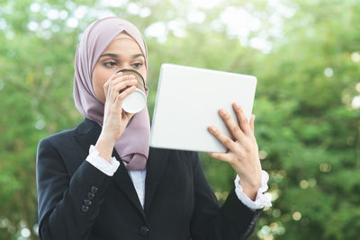 Businesswoman drinking coffee while holding digital tablet