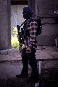 Young man holding rifle wearing mask standing in corridor