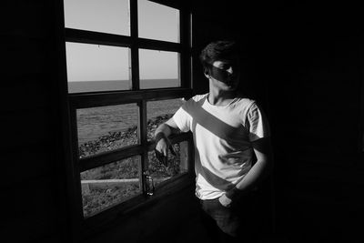 View of young man looking away while standing by window