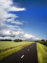 Road amidst field against blue sky