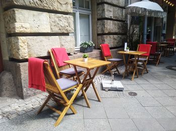 Empty chairs and tables at sidewalk cafe against building