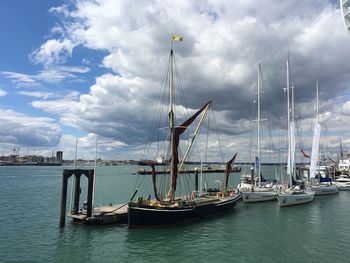 Sailboats moored on harbor against sky