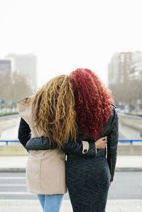 Rear view of lesbian couple with arms around standing against clear sky in city