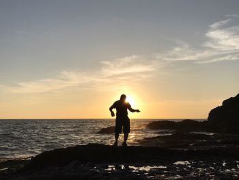 Silhouette man standing on rock at beach against sky during sunset