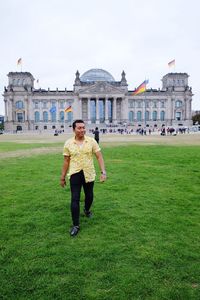 Full length of happy man walking on grassy field against the reichstag