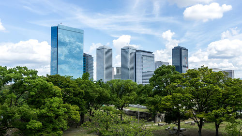 Trees and buildings in city against sky