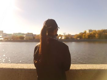 Woman standing by river in city against sky