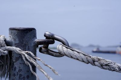 Close-up of rope tied on metal chain against sky