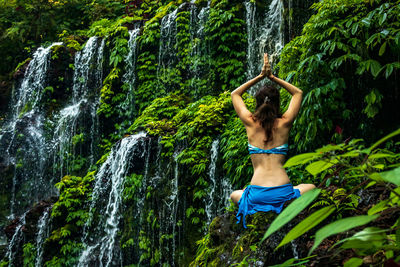 Rear view of woman meditating against waterfall