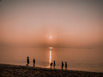Silhouette people on beach against sky during sunset