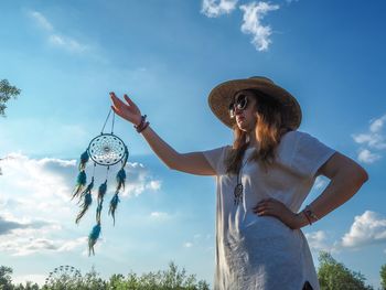 Woman holding dreamcatcher against sky