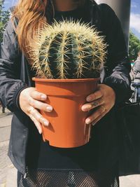 Midsection of woman holding potted cactus on footpath