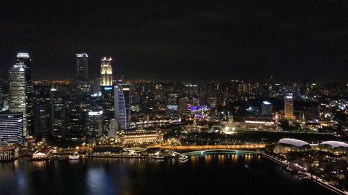 Illuminated buildings by river against sky at night